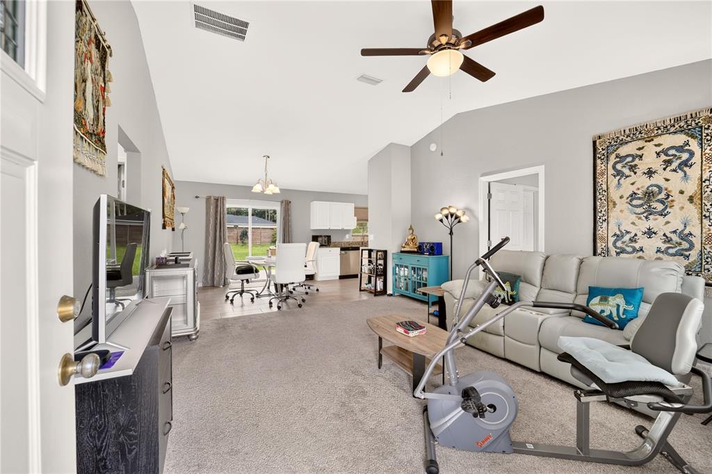 A living room with gray carpet, a ceiling fan, and a stationary bike near a sofa — 12203 SE 87TH COURT, BELLEVIEW, FL
