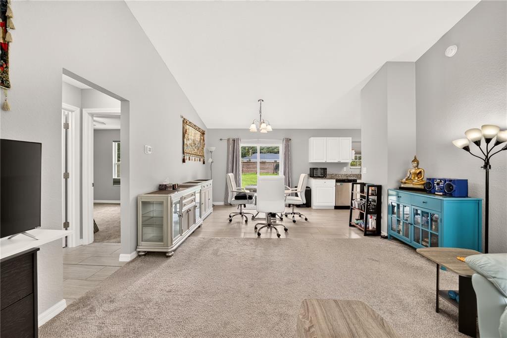 A living room with carpeted flooring transitions into a dining area with tile floors — 12203 SE 87TH COURT, BELLEVIEW, FL