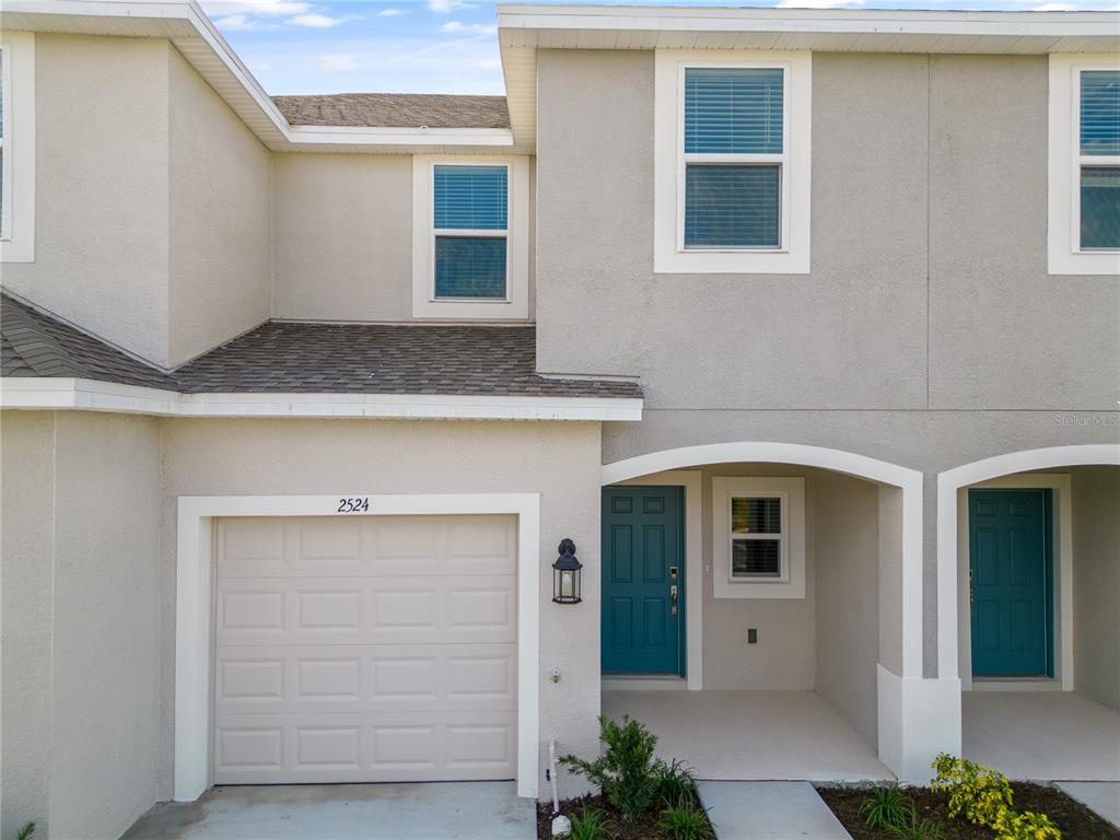 The exterior of a two-story townhouse features a garage, a blue front door, and stucco siding — 2415 PARAVANE WAY, WESLEY CHAPEL, FL