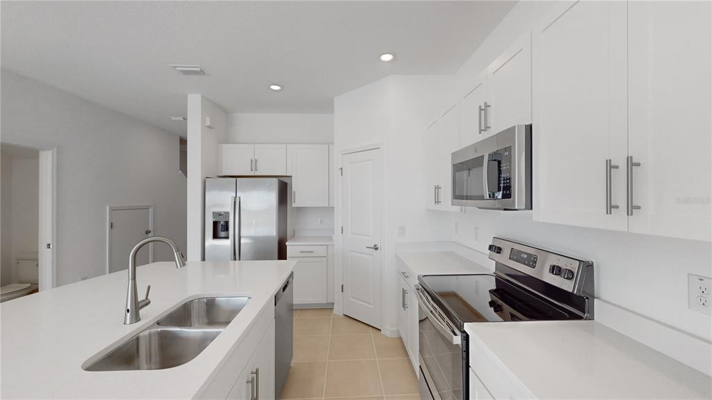 A modern kitchen features white cabinetry, stainless steel appliances, and a large central island — 2415 PARAVANE WAY, WESLEY CHAPEL, FL