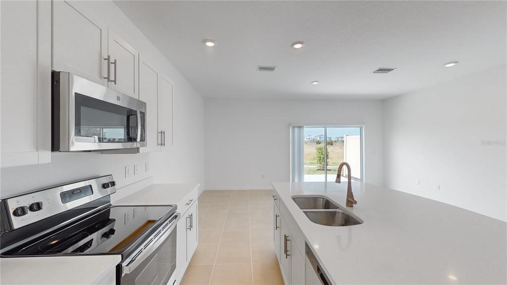A kitchen with white cabinets, stainless steel appliances, and a central island with a sink — 2415 PARAVANE WAY, WESLEY CHAPEL, FL