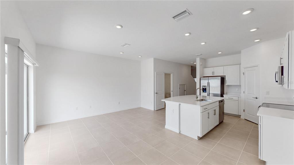 A bright, open-concept kitchen and living area features white cabinetry, an island, and tile flooring — 2415 PARAVANE WAY, WESLEY CHAPEL, FL