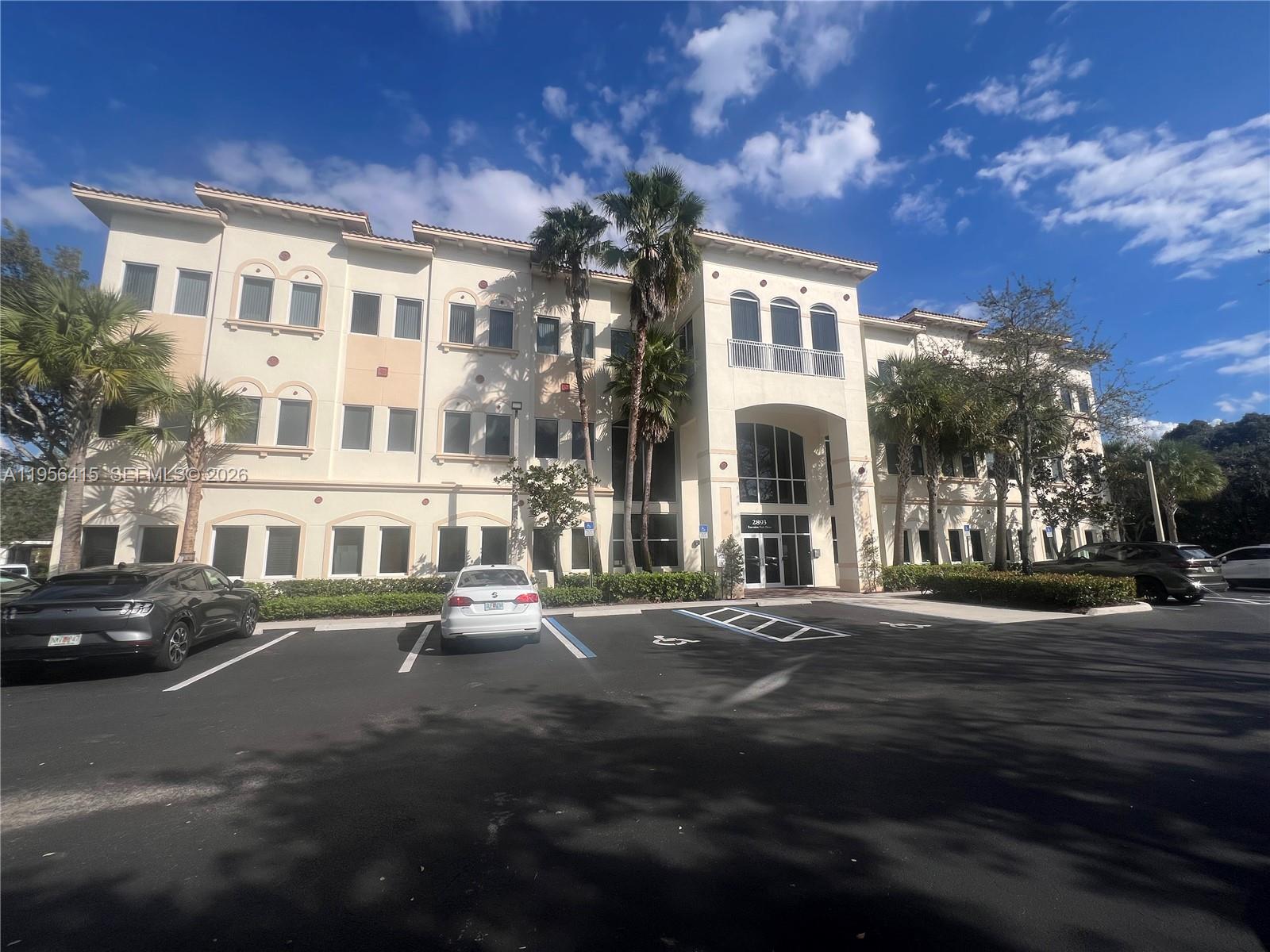 A three-story beige commercial building with a parking lot and palm trees in front — 2893 Executive Park Dr # 125, Weston FL 33331, WESTON, FL