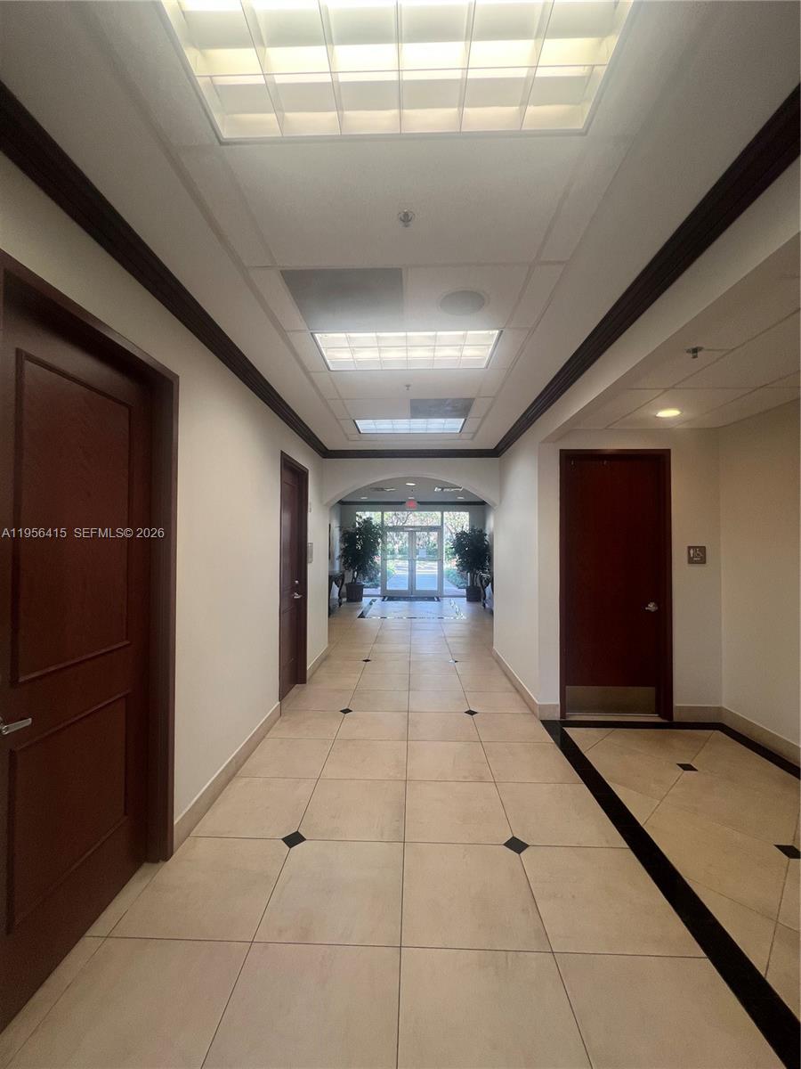 A tiled hallway with dark wood doors leads toward a glass-paned exterior entrance — 2893 Executive Park Dr # 125, Weston FL 33331, WESTON, FL