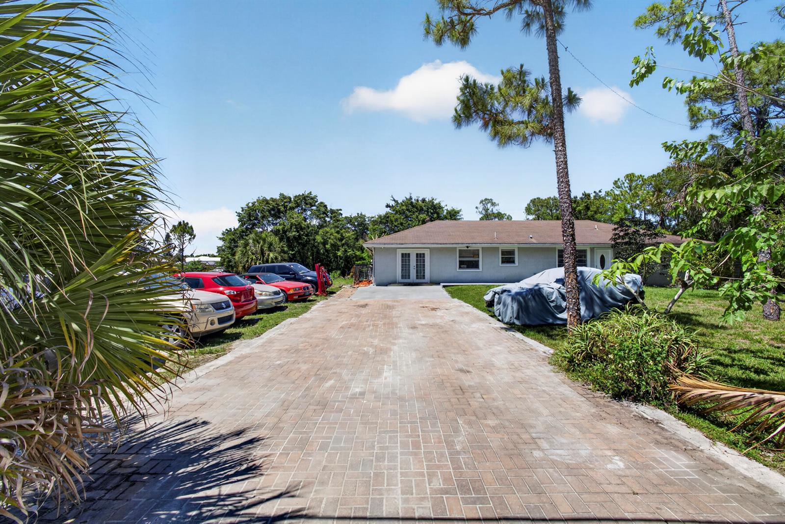 A paved driveway leads to a single-story house with several parked cars and trees — 16663 89th Place N, FL 33470, FL