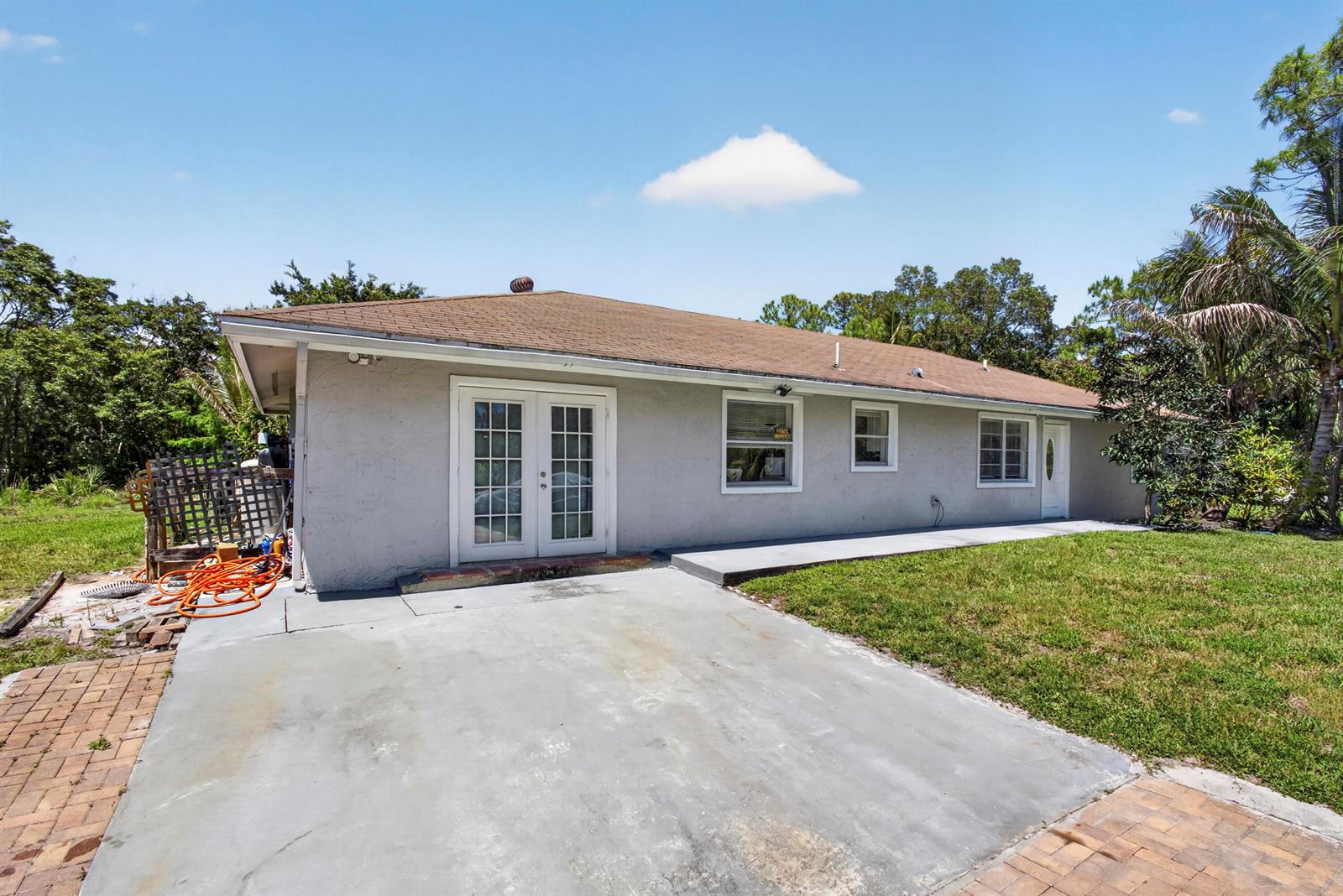 The exterior of a single-story house features a concrete patio, French doors, and a lawn — 16663 89th Place N, FL 33470, FL