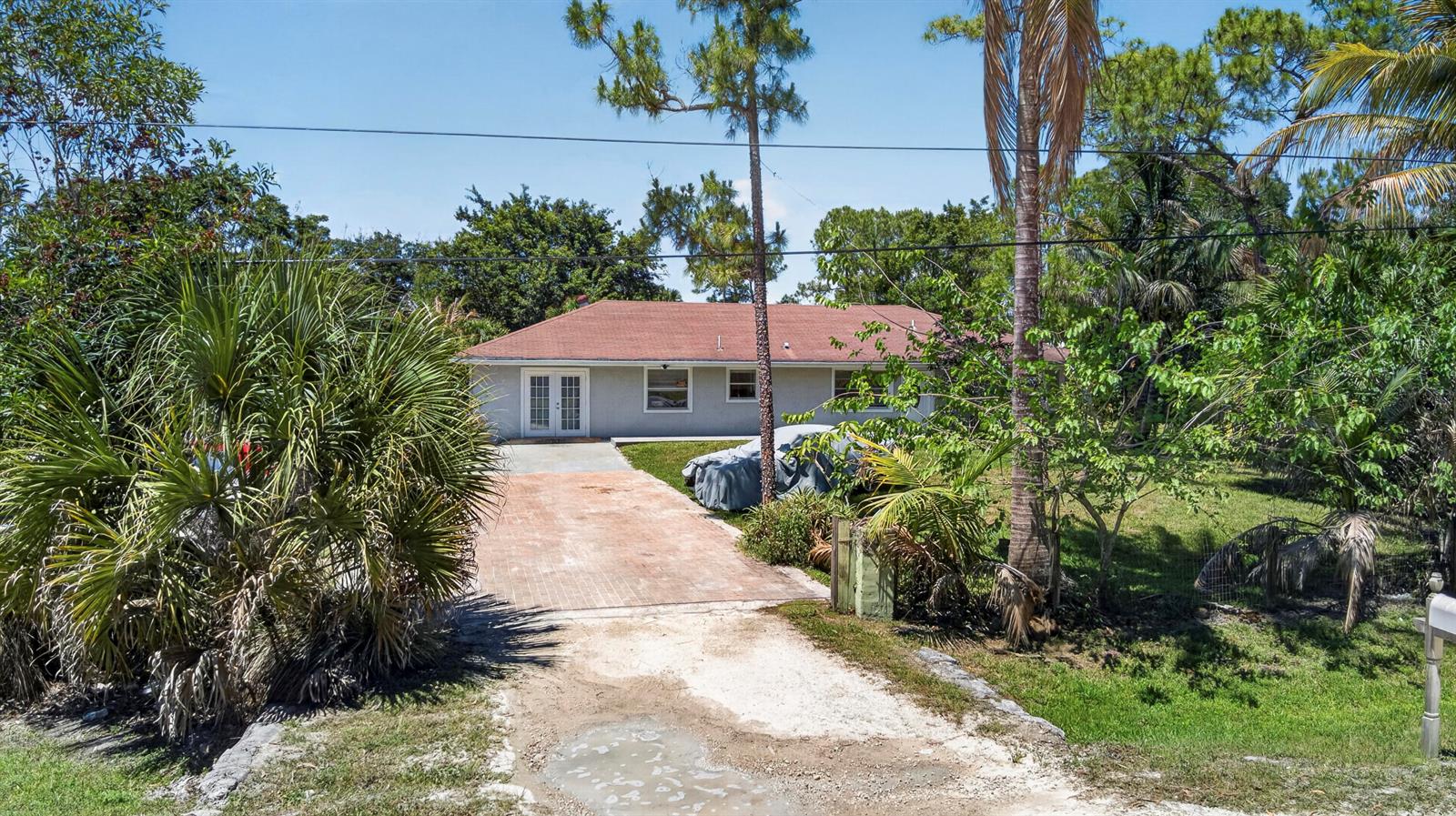 A single-story house with a red roof and a brick driveway sits among lush trees — 16663 89th Place N, FL 33470, FL
