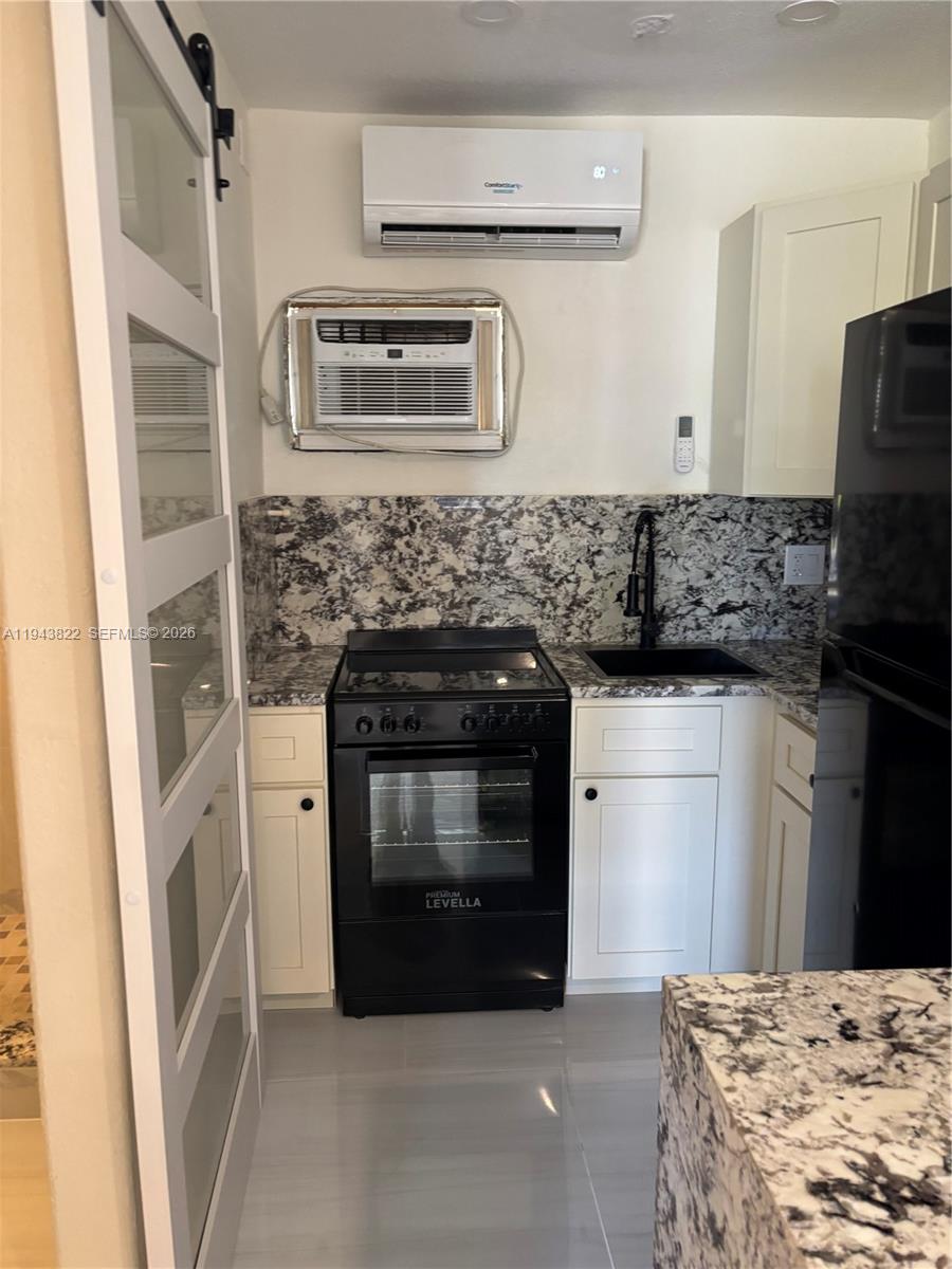 A small kitchen features black appliances, granite countertops, and both a wall and mini-split AC — 103365 Overseas Hwy # C, Key Largo FL 33037, KEY LARGO, FL
