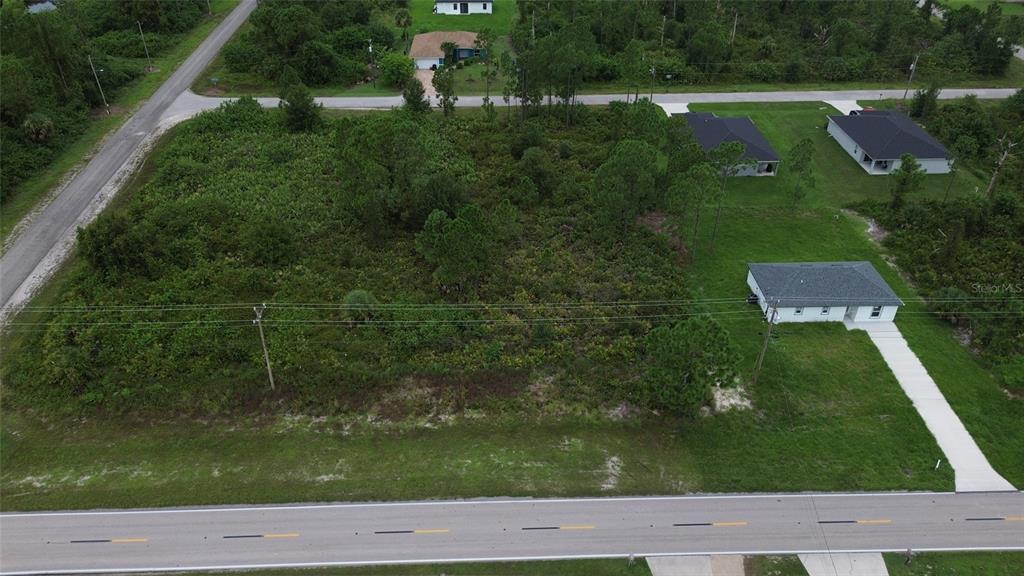 An aerial view shows a vacant, wooded lot situated between a paved road and a house — 464 COLUMBUS BLVD, LEHIGH ACRES, FL