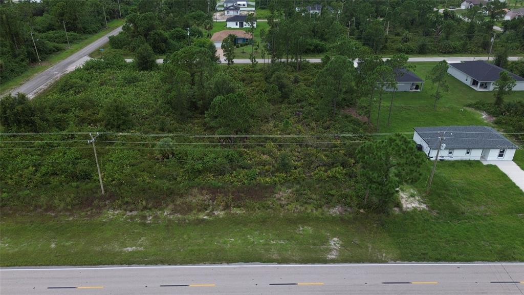 An aerial view shows a vacant, wooded residential lot situated between two existing houses — 464 COLUMBUS BLVD, LEHIGH ACRES, FL