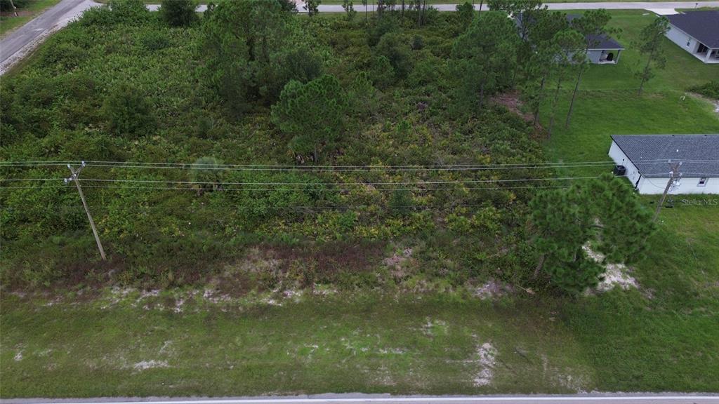 An aerial view shows a vacant, wooded residential lot situated between two houses — 464 COLUMBUS BLVD, LEHIGH ACRES, FL