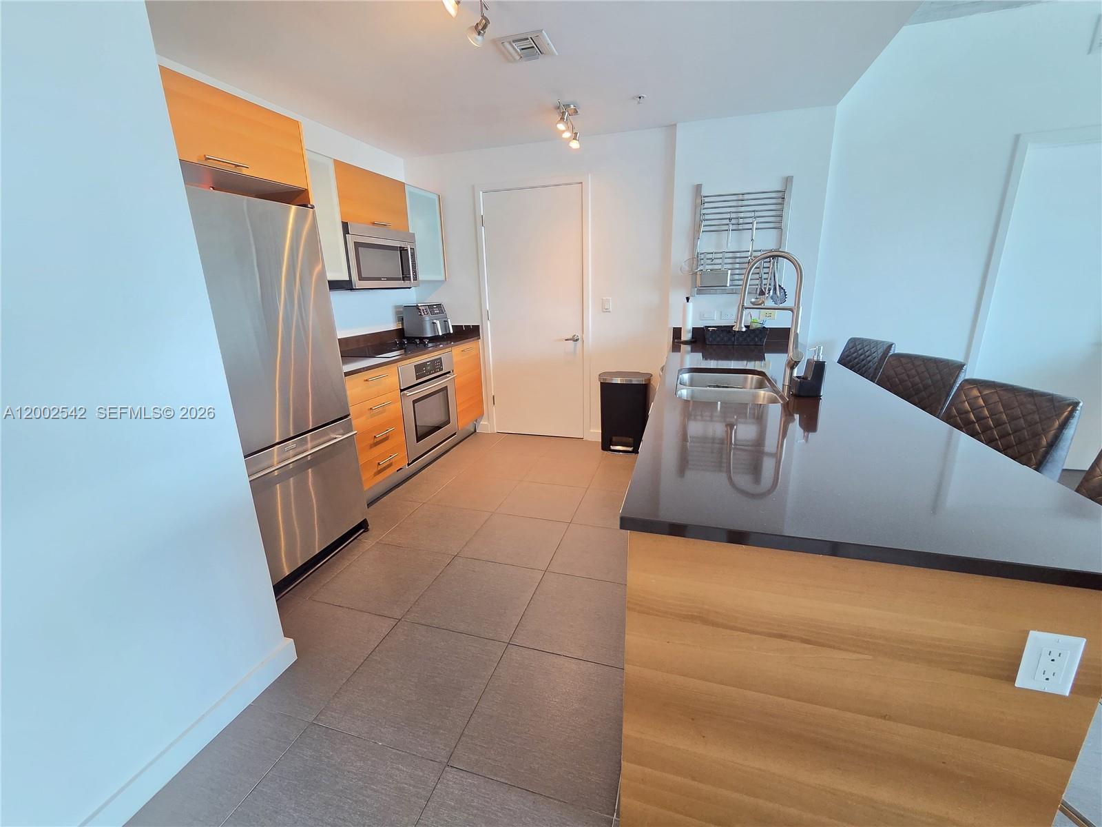 A modern kitchen features light wood cabinetry, stainless steel appliances, and a dark countertop island — 3301 NE 1st Ave # H2710, Miami FL 33137, MIAMI, FL