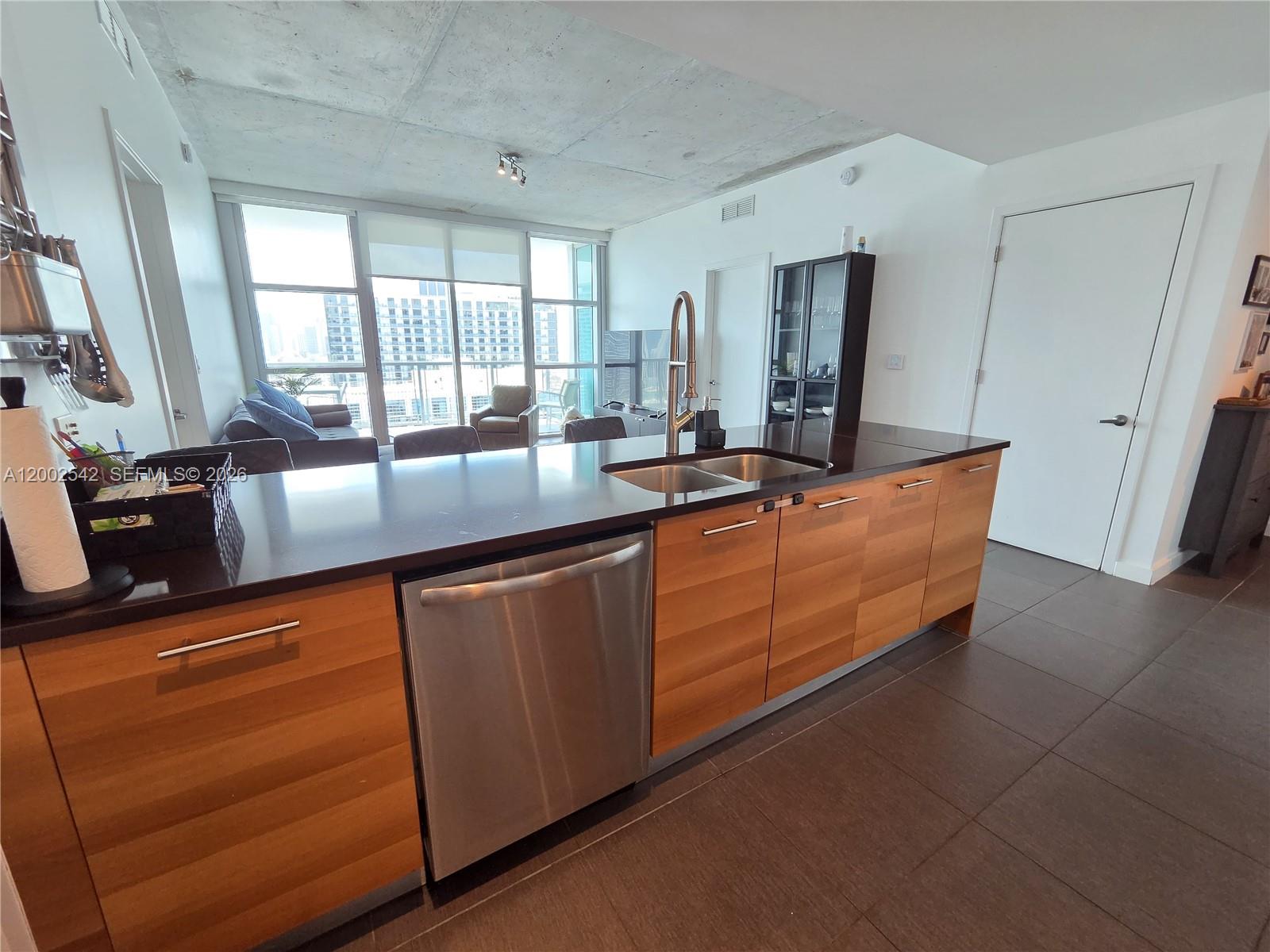 A modern kitchen features wood-grain cabinets, a stainless steel dishwasher, and a dark countertop — 3301 NE 1st Ave # H2710, Miami FL 33137, MIAMI, FL