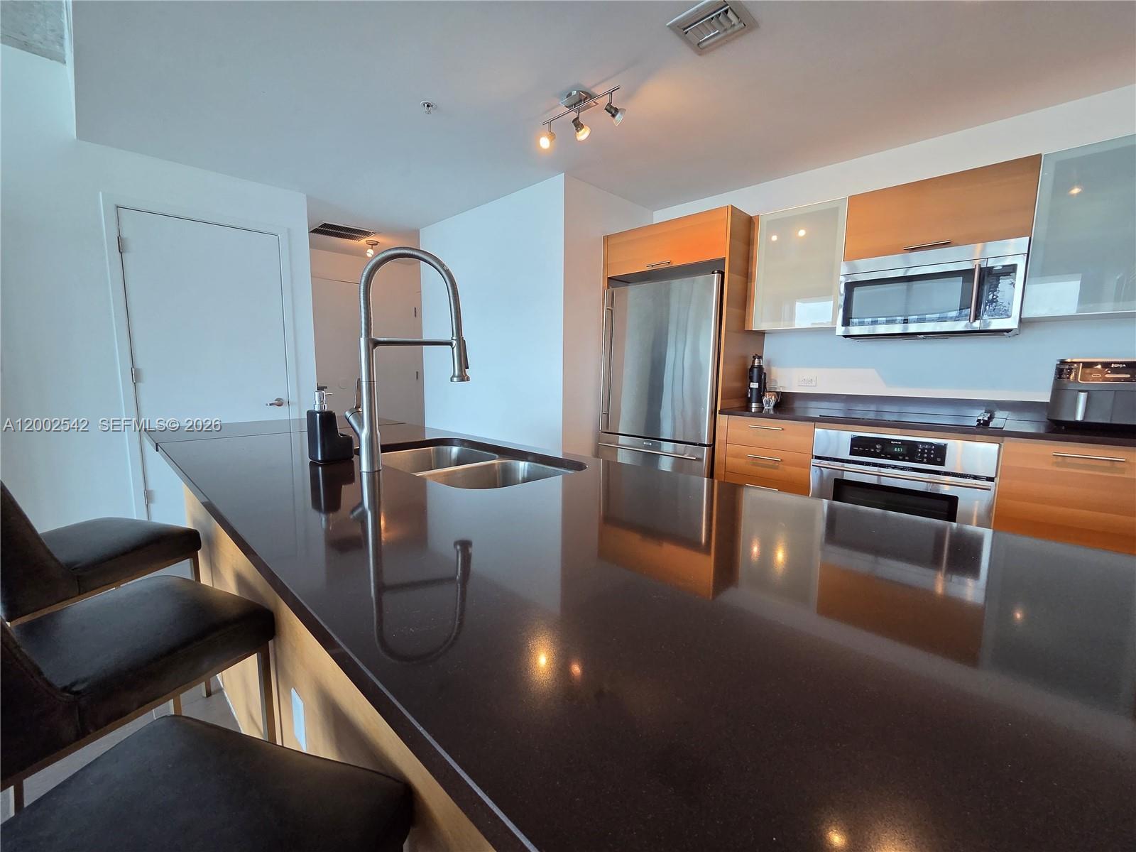 A modern kitchen features a dark countertop island, stainless steel appliances, and light wood cabinetry — 3301 NE 1st Ave # H2710, Miami FL 33137, MIAMI, FL