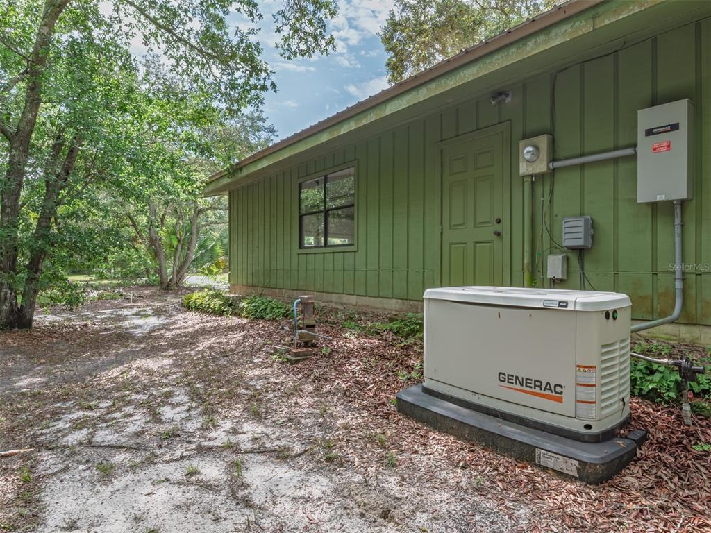 A Generac standby generator sits on a concrete pad outside a green-sided house — 17 S BAYSHORE DRIVE, EASTPOINT, FL
