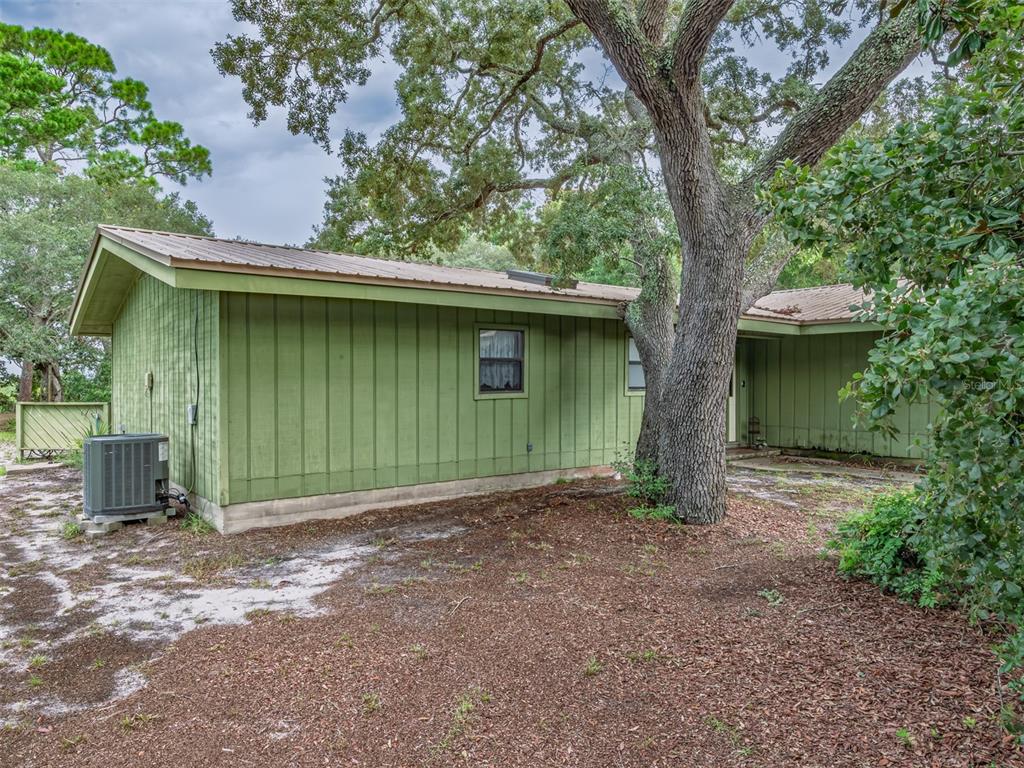 A green, single-story house with a metal roof sits among trees on a sandy lot — 17 S BAYSHORE DRIVE, EASTPOINT, FL