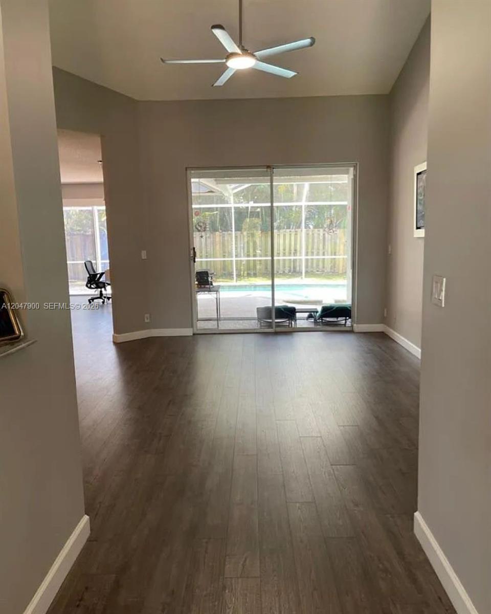 A living room with wood-look flooring, a ceiling fan, and sliding doors leading to a pool — 10644 Edinburgh St, Cooper City FL 33026, COOPER CITY, FL