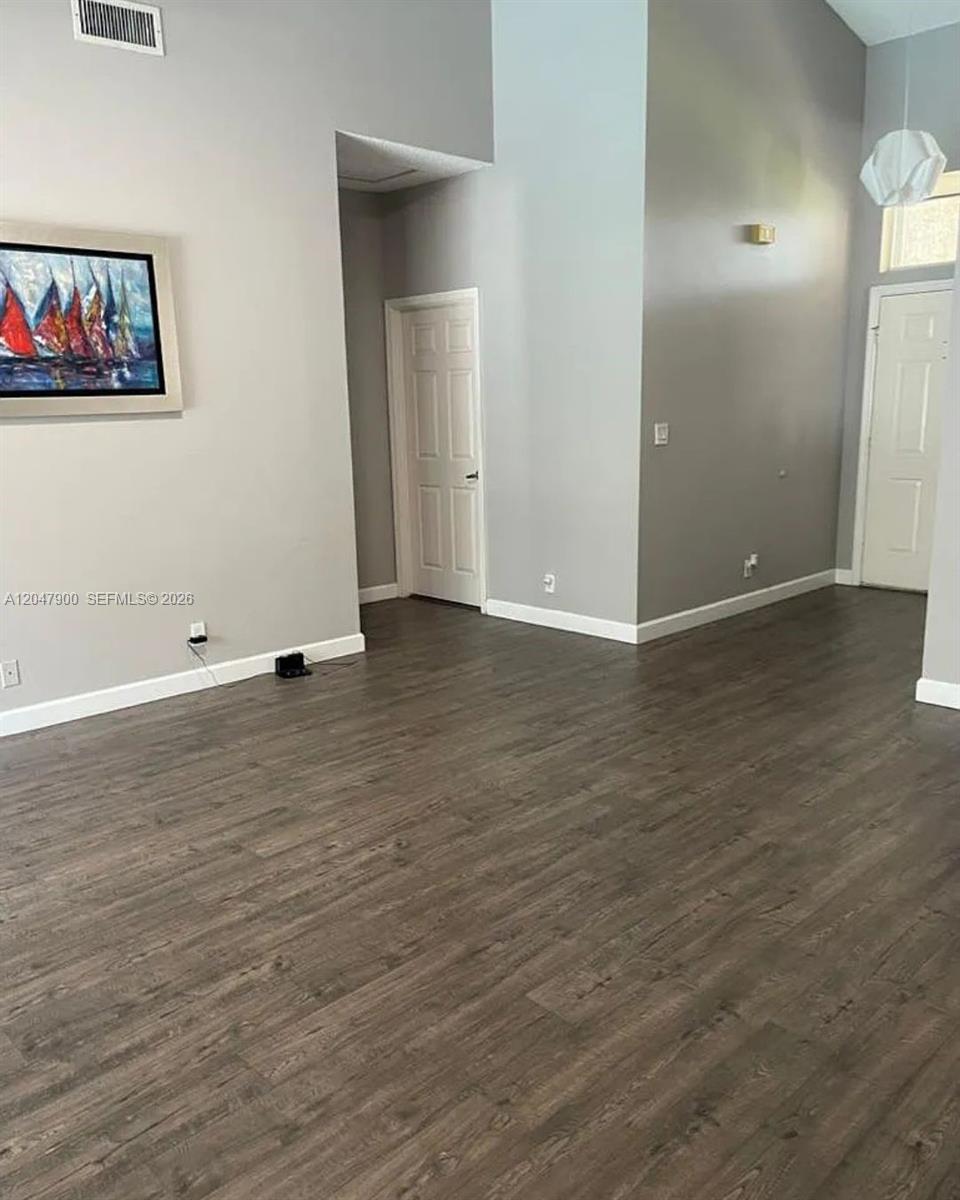 An empty room features gray walls, dark wood-look flooring, and a white interior door — 10644 Edinburgh St, Cooper City FL 33026, COOPER CITY, FL