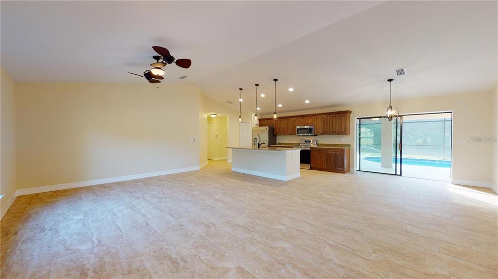 An open-concept kitchen and living area features tile flooring, wood cabinets, and a pool view — 2337 SIMONTON AVENUE, NORTH PORT, FL