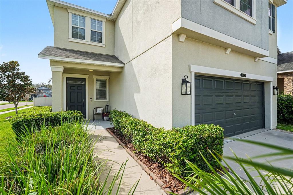 A two-story house exterior features a dark garage door, a front entrance, and landscaped hedges — 8165 FAIRE FROST LANE, LAND O LAKES, FL