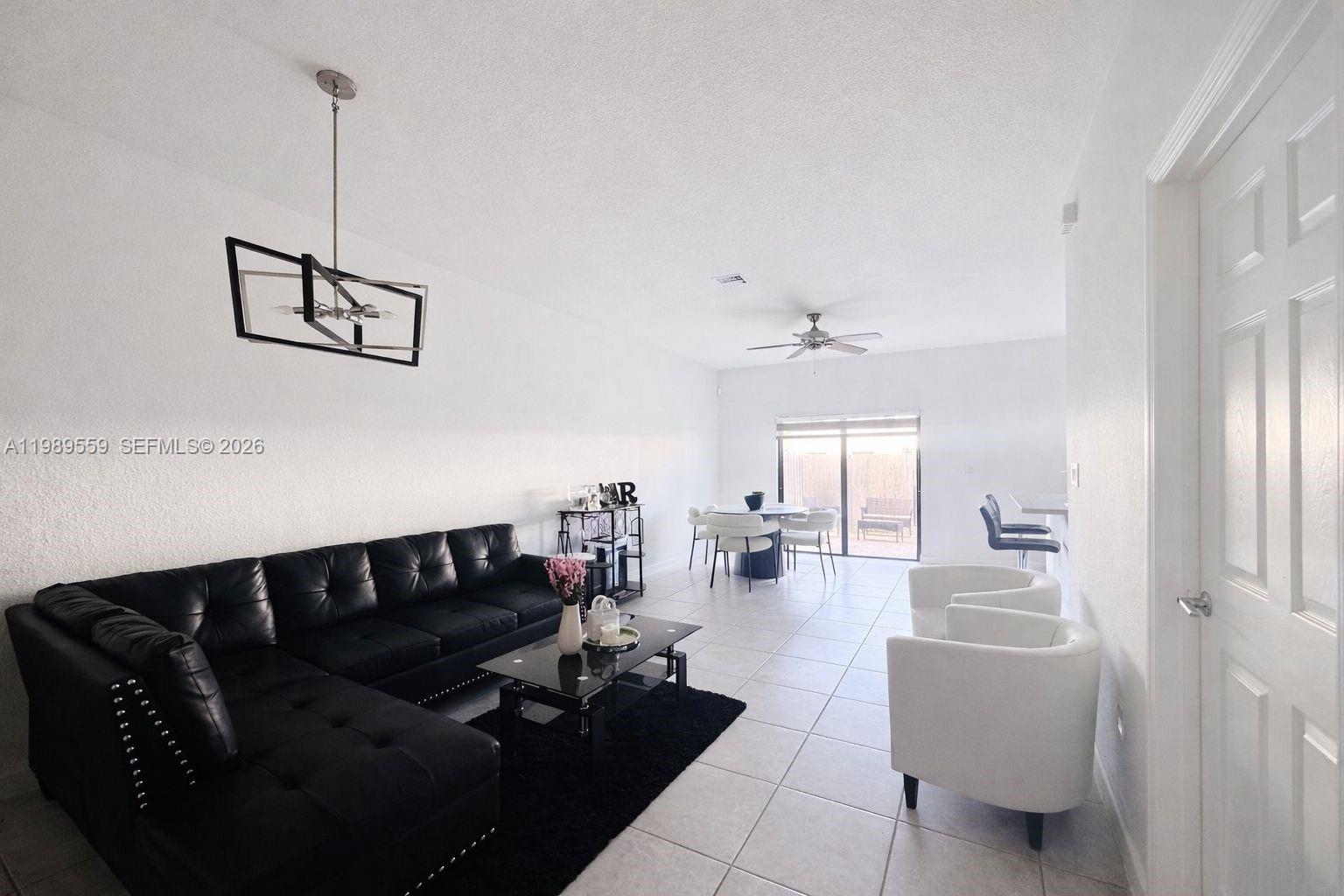 A living and dining area features a black sectional sofa, white chairs, and tile flooring — 12767 SW 230th Ter, Miami FL 33170, MIAMI, FL