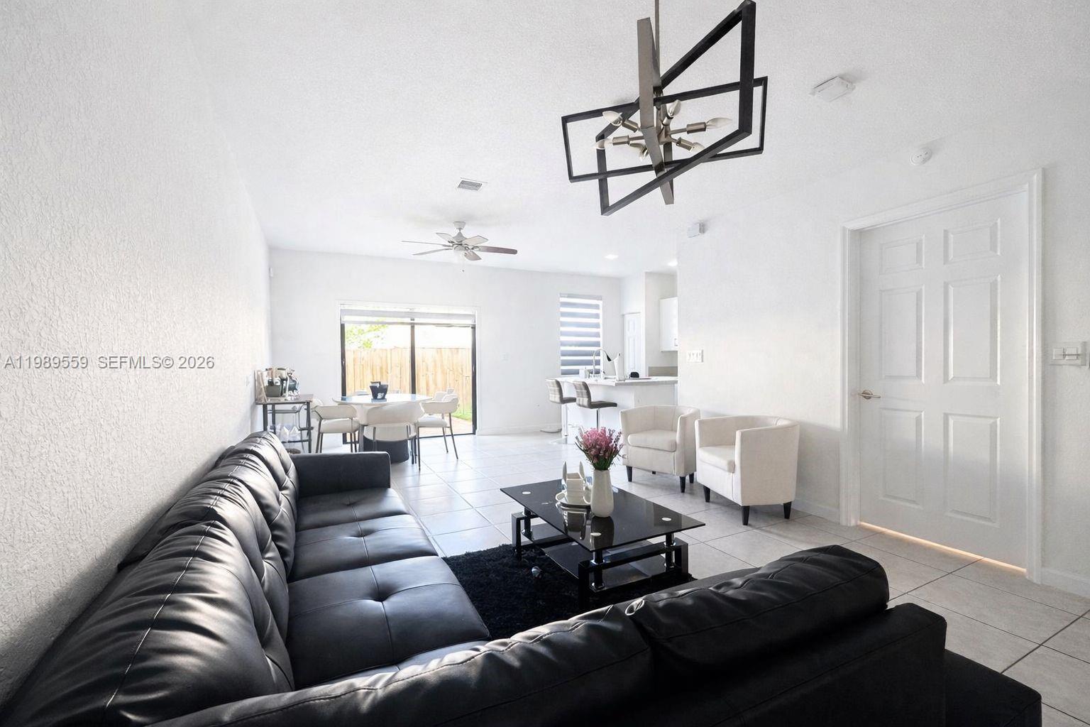This living room features a black leather sofa, a glass coffee table, and tile flooring — 12767 SW 230th Ter, Miami FL 33170, MIAMI, FL