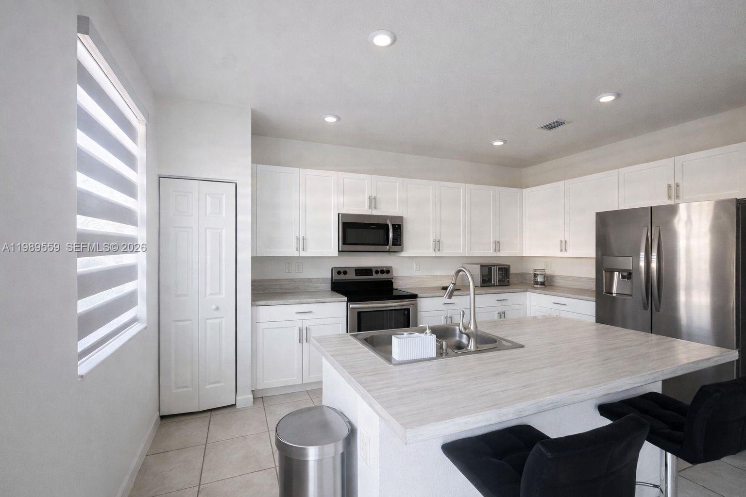 A modern kitchen features white cabinetry, stainless steel appliances, and a light-colored island countertop — 12767 SW 230th Ter, Miami FL 33170, MIAMI, FL