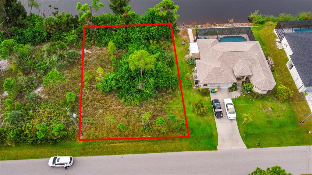 An aerial view shows a vacant, rectangular lot outlined in red next to a house — 15149 AMSTERDAM AVENUE, PORT CHARLOTTE, FL