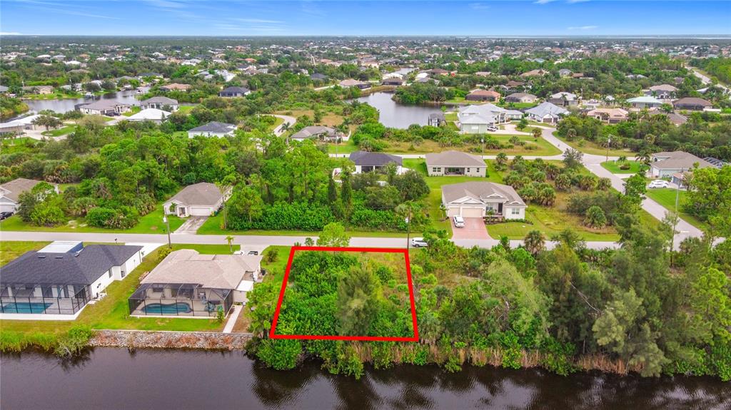 An aerial view shows a vacant, rectangular lot outlined in red bordering a canal — 15149 AMSTERDAM AVENUE, PORT CHARLOTTE, FL