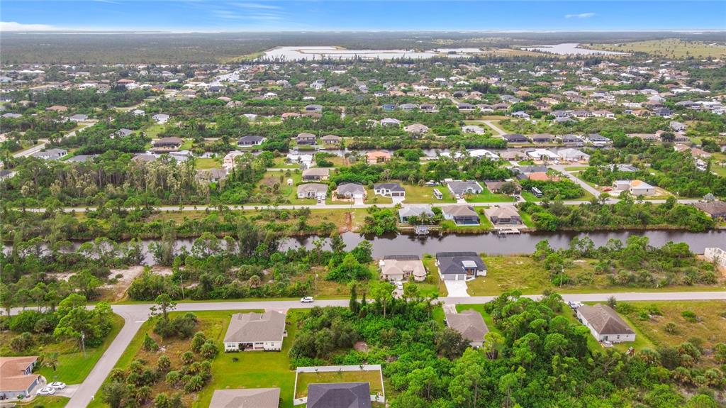 An aerial view shows a suburban neighborhood with houses, a canal, and surrounding green space — 15149 AMSTERDAM AVENUE, PORT CHARLOTTE, FL