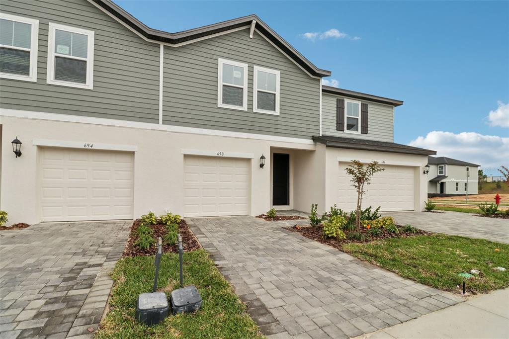A row of townhouses features beige stucco lower levels, green siding, and paved driveways — 690 MUHLY WAY, LADY LAKE, FL