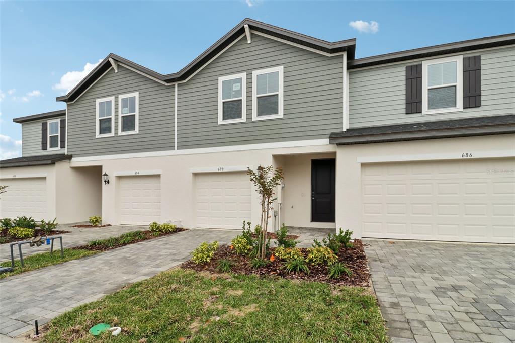 The exterior of a multi-unit townhouse complex features gray siding, white stucco, and garage doors — 690 MUHLY WAY, LADY LAKE, FL