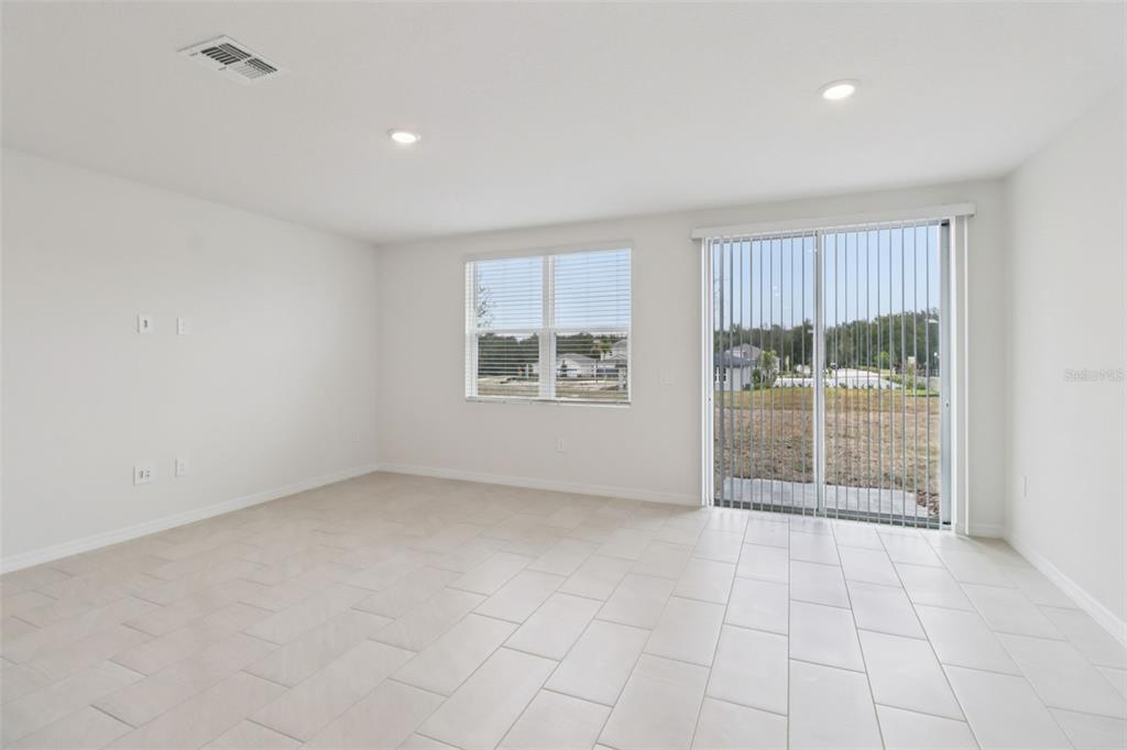 An empty room with white walls, tile flooring, a window, and sliding glass doors — 690 MUHLY WAY, LADY LAKE, FL