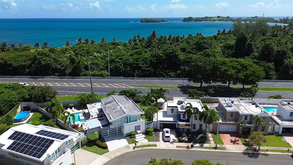 An aerial view shows a row of modern houses with swimming pools near a coastal highway — 14 VIA CANGREJOS, TOA BAJA, PR