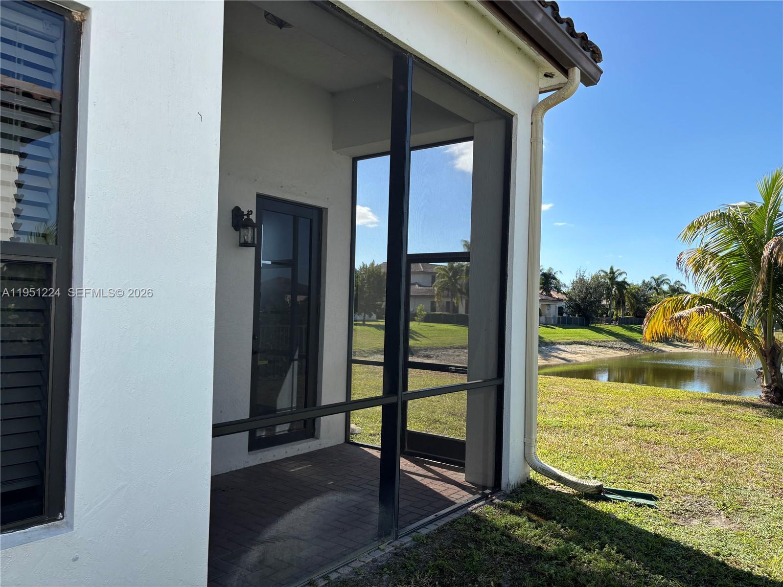 A screened-in patio features brick pavers, a glass door, and views of a pond — 4783 Rosetta Terrace, Ave Maria FL 34142, AVE MARIA, FL