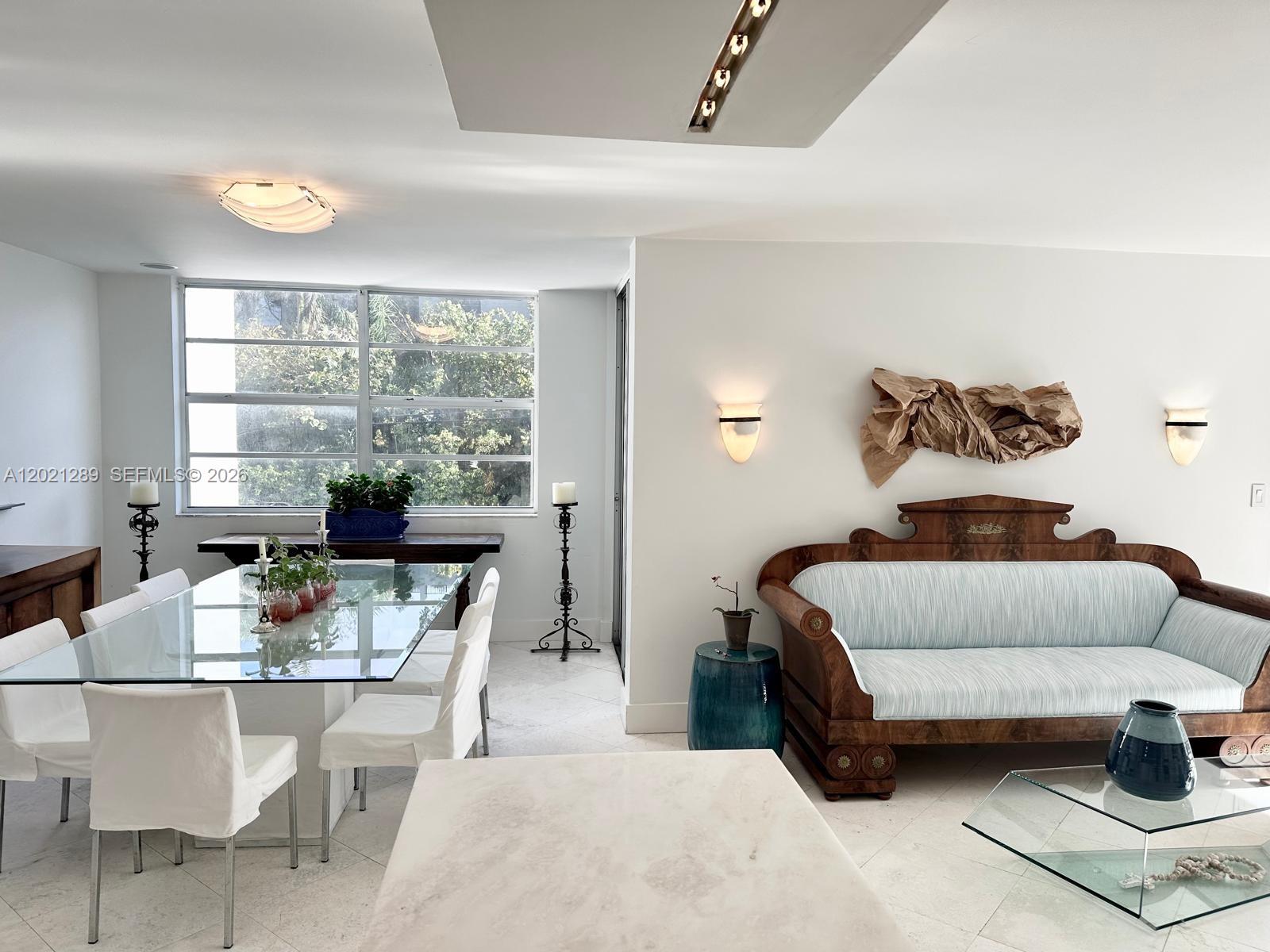 A dining area with a glass table and a living space featuring a wooden sofa — 150 Ocean Lane Dr # 2A, Key Biscayne FL 33149, KEY BISCAYNE, FL