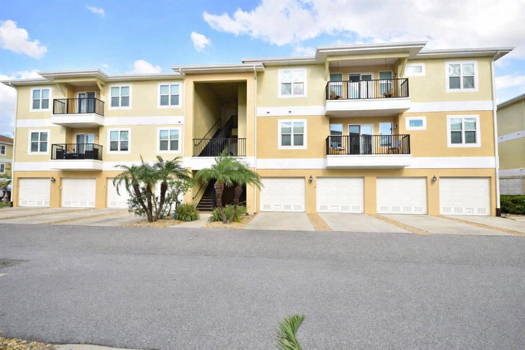 A three-story apartment building with balconies and ground-level garages under a blue sky — 6420 BANYAN BOULEVARD UNIT 303, NEW PORT RICHEY, FL
