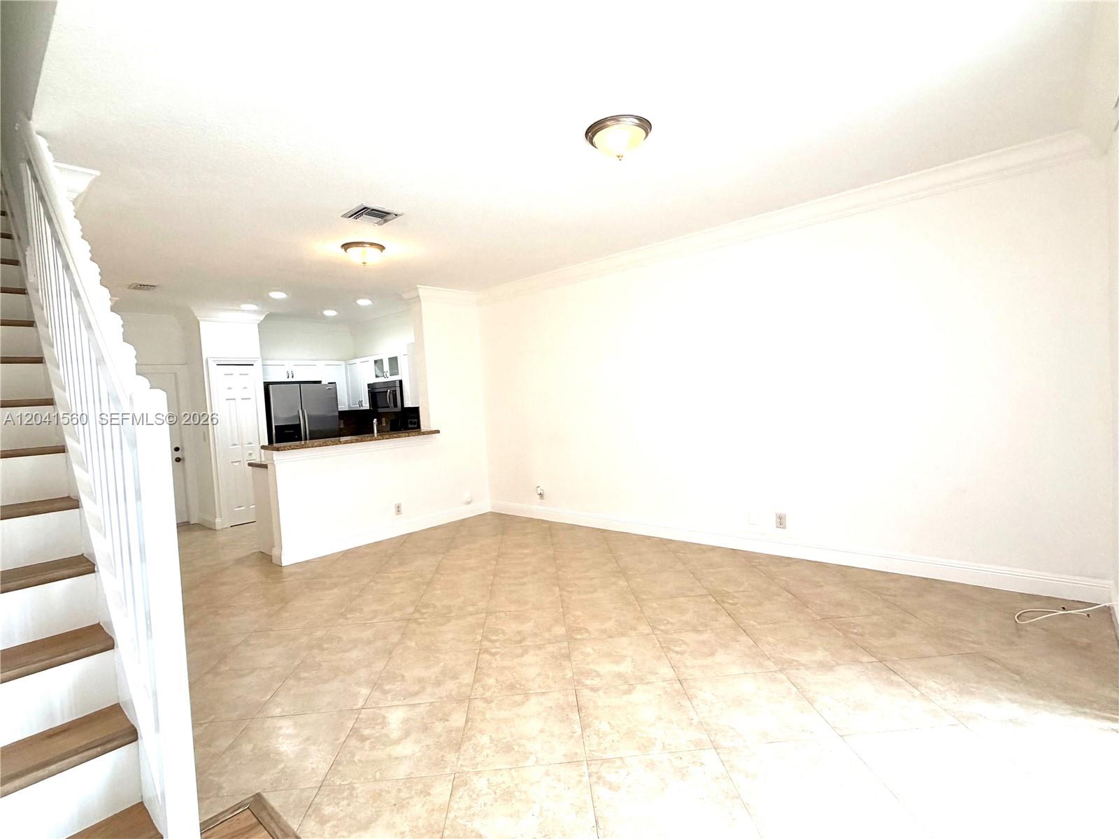 An open-concept living area features tile flooring, a staircase, and a kitchen with white cabinets — 2560 Cordoba Bnd # 2560, Weston FL 33327, WESTON, FL