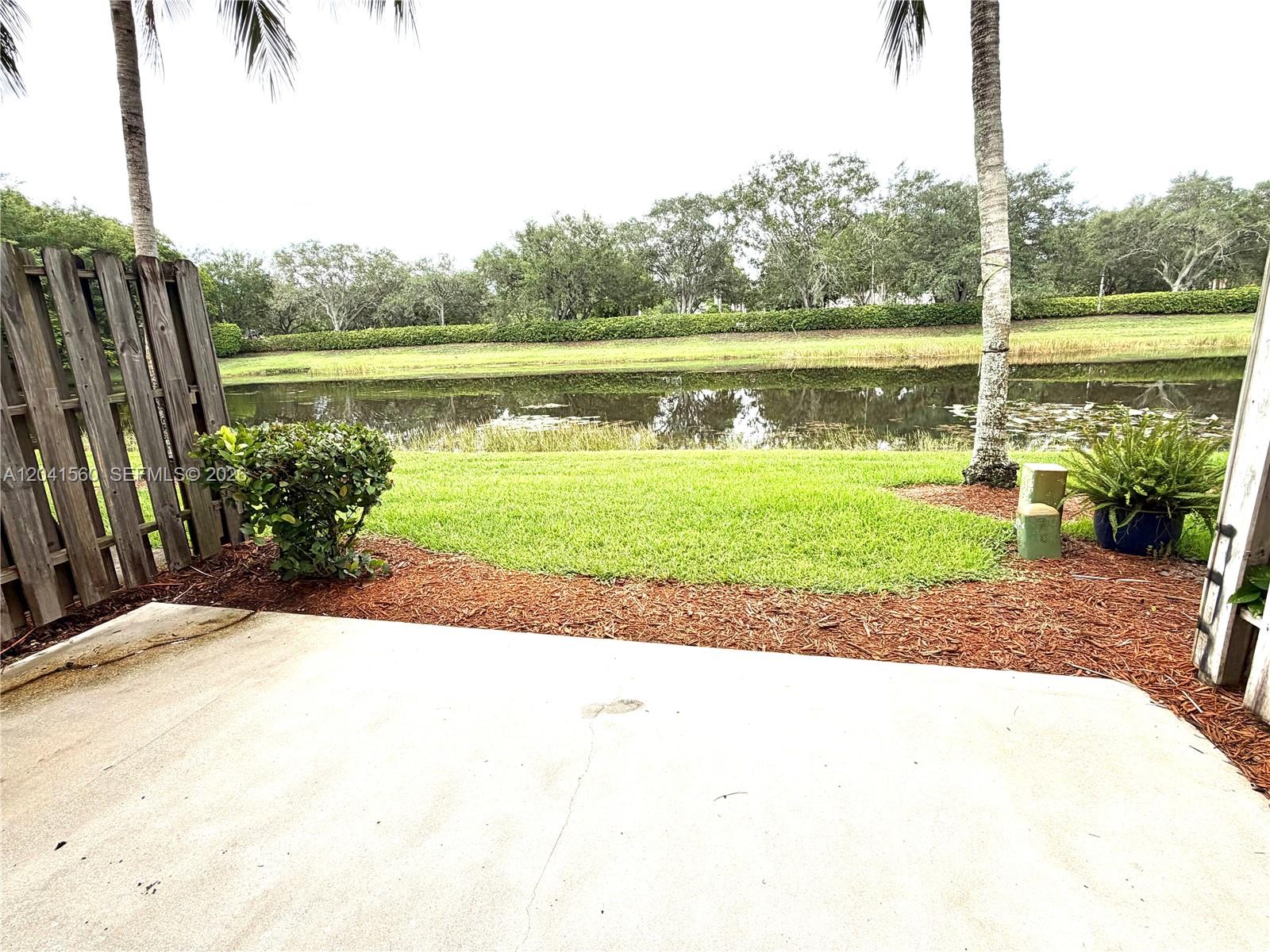 A concrete patio overlooks a grassy lawn, a pond, and a line of trees — 2560 Cordoba Bnd # 2560, Weston FL 33327, WESTON, FL