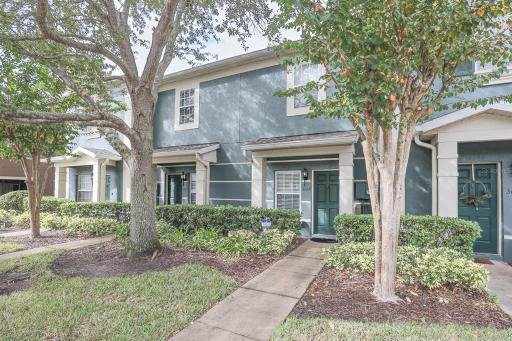 A row of two-story townhomes with dark green doors, concrete walkways, and mature landscaping — 3664 WILSHIRE WAY ROAD UNIT 261, ORLANDO, FL