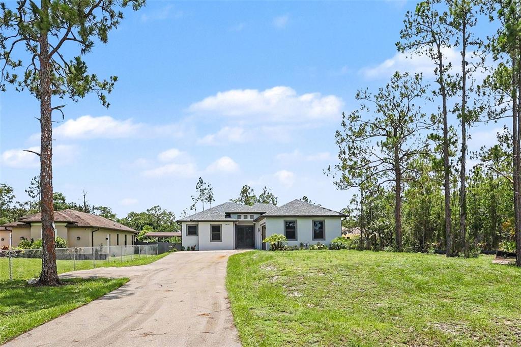 A single-story house with a paved driveway sits on a grassy lot with pine trees — 2420 52ND AVENUE NE, NAPLES, FL