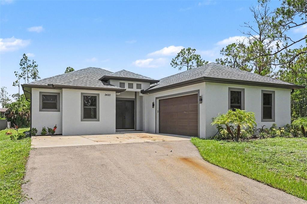 A single-story house with a white stucco exterior, gray trim, and an attached two-car garage — 2420 52ND AVENUE NE, NAPLES, FL