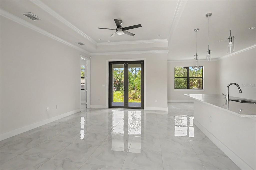 A bright, open-concept living area features white tile floors, a tray ceiling, and glass doors — 2420 52ND AVENUE NE, NAPLES, FL