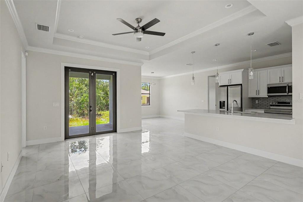 A bright, open-concept living area with white tile floors, a tray ceiling, and a modern kitchen — 2420 52ND AVENUE NE, NAPLES, FL