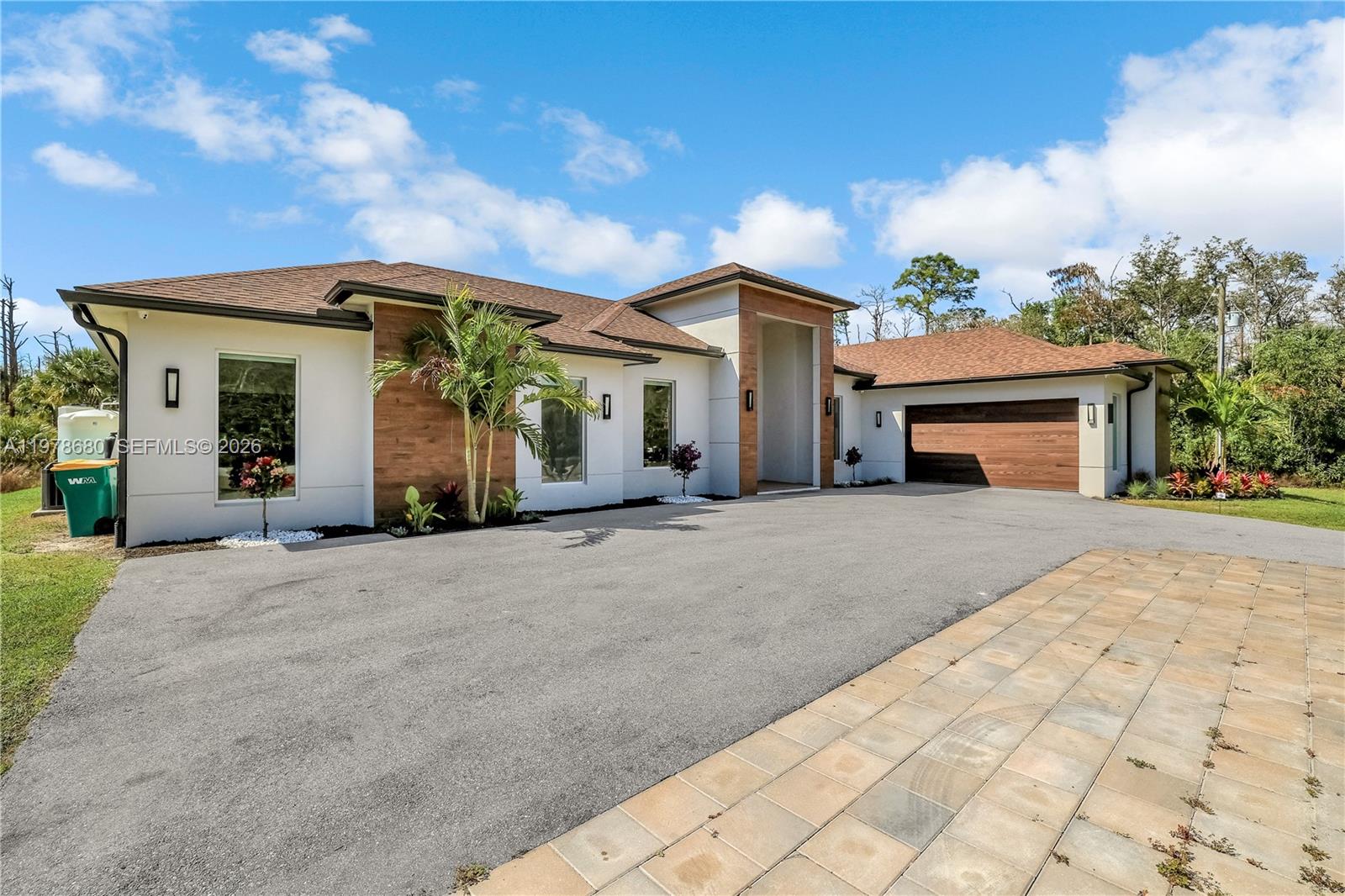 A modern single-story house with a wood-accented facade, attached garage, and paved driveway — 1899 Wilson Blvd N, Naples FL 34120, NAPLES, FL