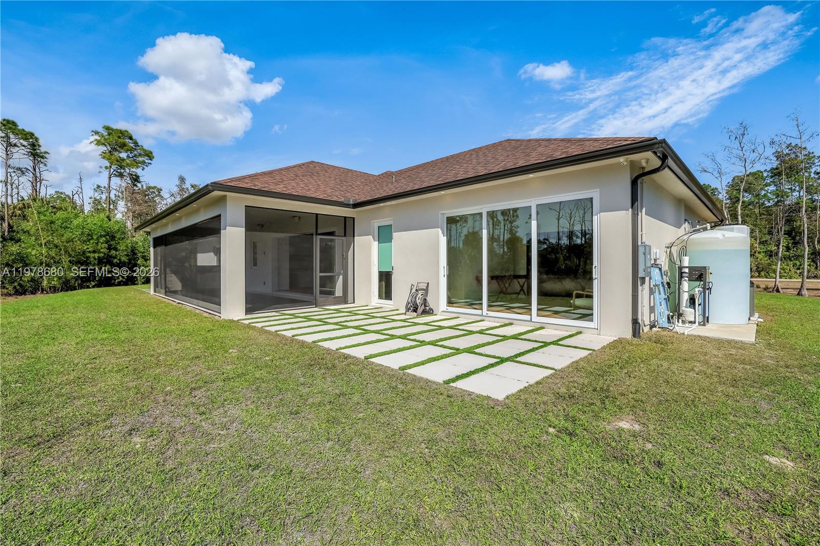 A backyard view shows a house with a screened patio, sliding glass doors, and a water tank — 1899 Wilson Blvd N, Naples FL 34120, NAPLES, FL