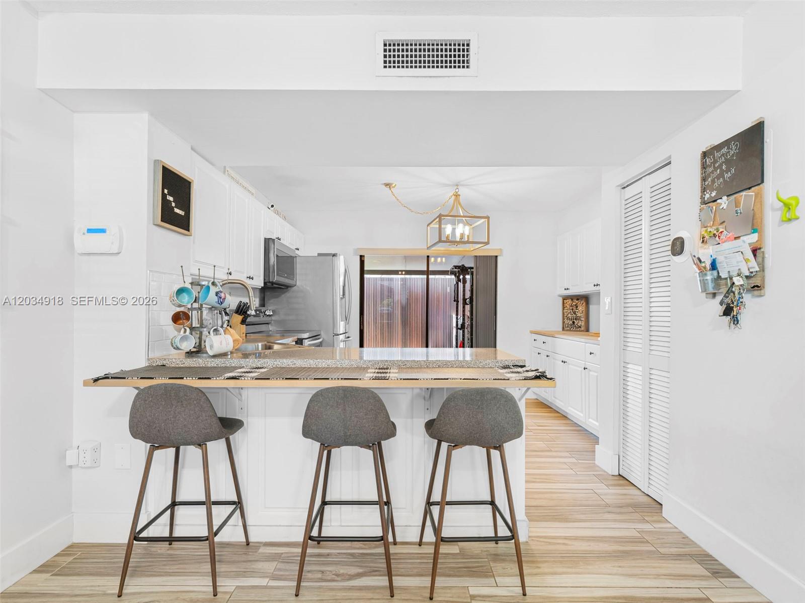 A kitchen features a breakfast bar with three stools, white cabinetry, and wood-look tile flooring — 1805 SW 107th Ave # 2601, Miami FL 33165, MIAMI, FL