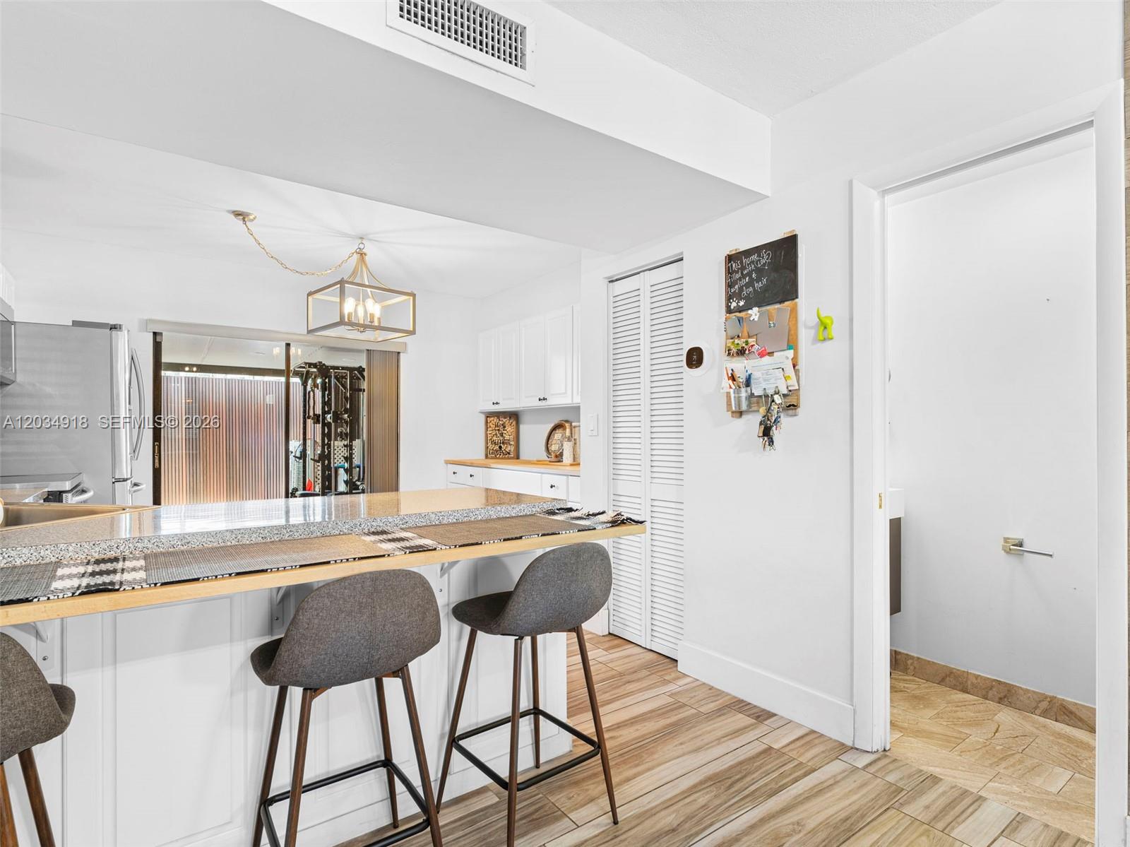 A kitchen features a breakfast bar with stools, white cabinets, and light wood-look flooring — 1805 SW 107th Ave # 2601, Miami FL 33165, MIAMI, FL