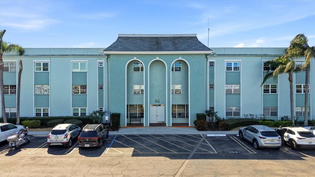 A three-story, light blue apartment building features a central arched entryway and a parking lot — 1706 BELLEAIR FOREST DRIVE UNIT 128, BELLEAIR, FL