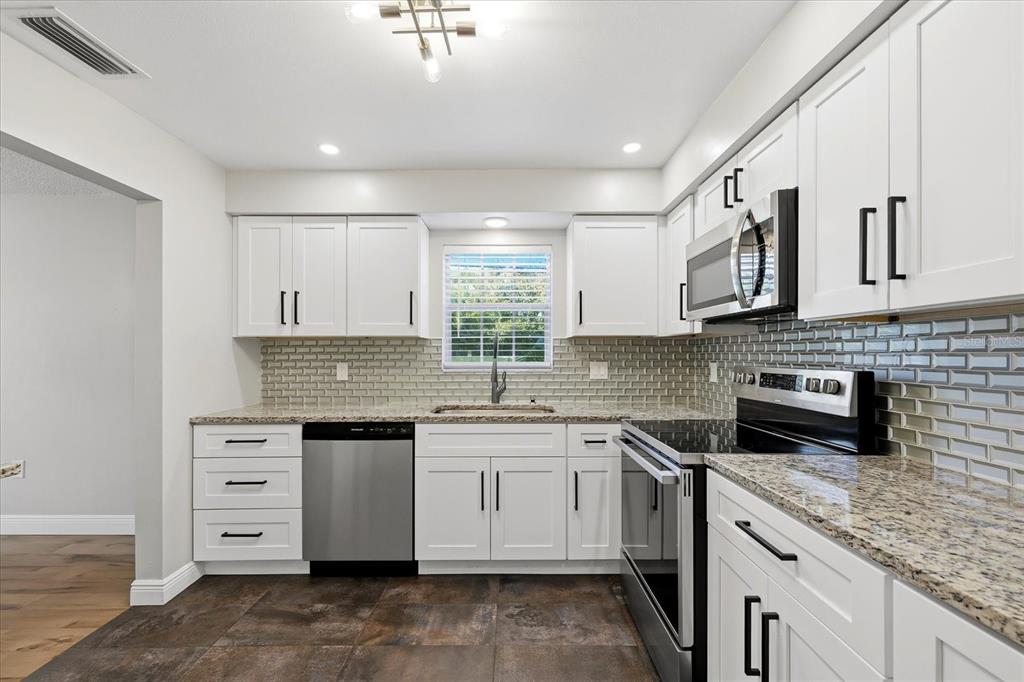 A kitchen with white cabinets, stainless steel appliances, granite countertops, and a gray subway tile backsplash — 1706 BELLEAIR FOREST DRIVE UNIT 128, BELLEAIR, FL